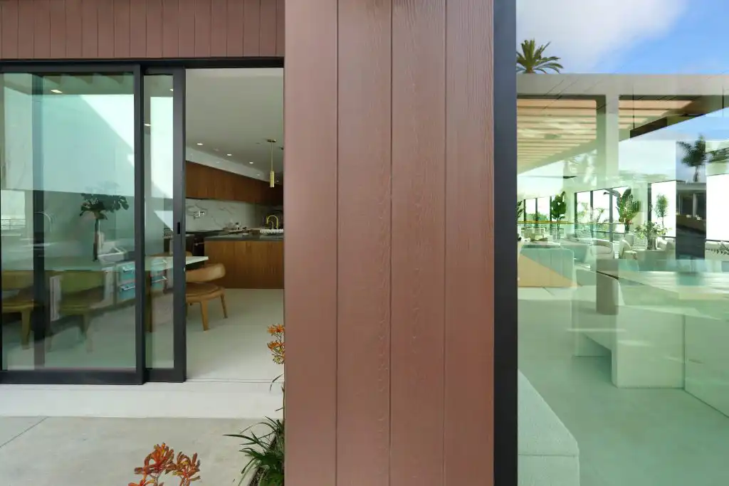 ACRE nickel gap siding installed vertically in warm brown stain on luxury home exterior with floor-to-ceiling glass and pool