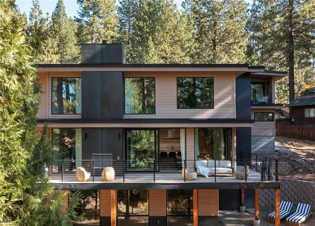 ACRE siding on a multi-level contemporary mountain home with large windows and outdoor living deck surrounded by pines