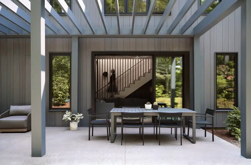 Covered outdoor dining area with gray composite vertical siding walls and open-frame steel pergola ceiling