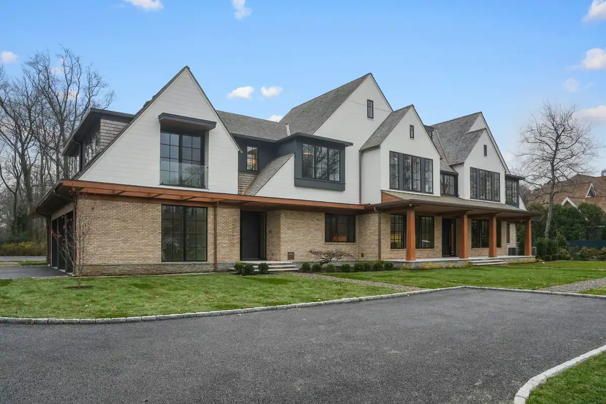Large home with white horizontal siding above a brick base, with wood column accents